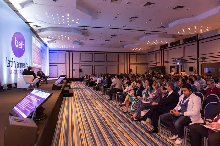 Plateia em auditório durante congresso, com telão do evento ao fundo