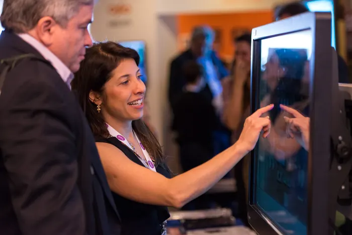 Participante interagindo com um monitor touchscreen em estande