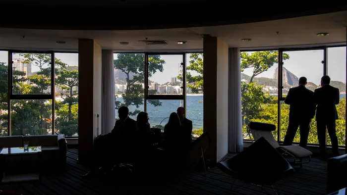 Silhuetas de pessoas em salão com grandes janelas e vista externa